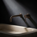 Fonte Wall-Mounted Basin Mixer 240mm in Cast Bronze above a carved travertine basin